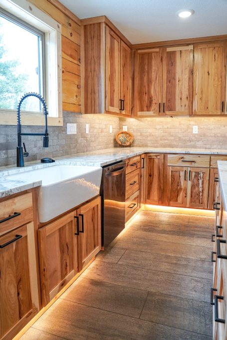 Rustic Hickory Cupboards and sink with white marbled countertops.